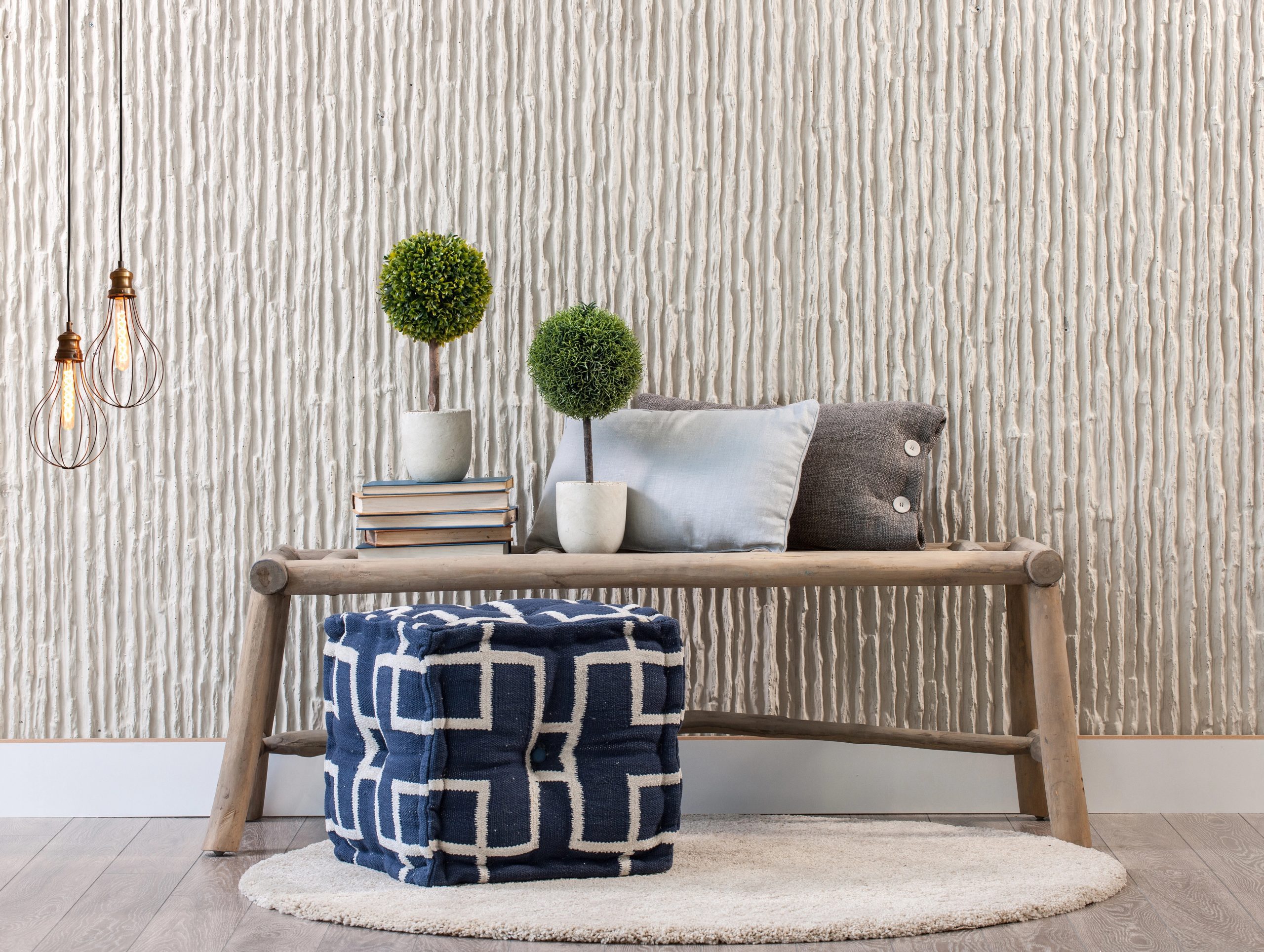 Cozy Airbnb Living Area Design by Kenchel Interior Design Airbnb living area featuring a wooden bench with decorative pillows, topiary accents, a patterned ottoman, and textured walls for a cozy and stylish design.